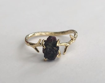 May include: A gold ring with a branch design and a dark red gemstone.