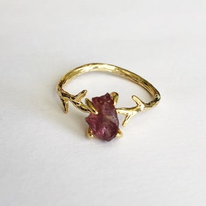 May include: A gold ring with a pink gemstone set in a branch design.