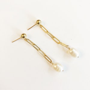 May include: A pair of gold chain earrings with a white pearl dangling from each chain.