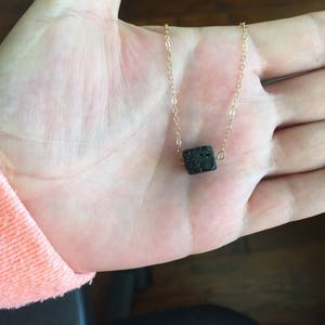 May include: A gold chain necklace with a black lava rock pendant.