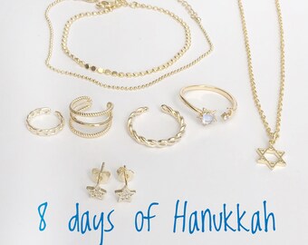 May include: A set of eight gold-toned jewelry pieces, including a necklace with a Star of David pendant, two bracelets, a ring with a moonstone, two earings, and two ear cuffs. The text "8 days of Hanukkah" is written in blue ink below the jewelry.
