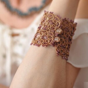 Peut inclure: Un bracelet délicat en dentelle de couleur or et violet. Le bracelet présente un motif floral et est orné de petites perles transparentes.
