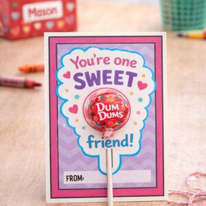 May include: A greeting card with a Dum Dums lollipop. The card has a pink and purple design with the words "You're one SWEET friend!" The lollipop is red and has a clear wrapper.
