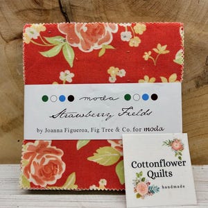 May include: A bundle of red fabric squares with a floral design, labelled "Strawberry Fields" by Joanna Figueroa. A small tag reads "Cottonflower Quilts, handmade."