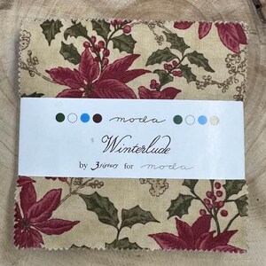 May include: A fabric square with a beige background and a floral pattern featuring red poinsettias, green leaves, and white berries. The fabric is labeled "Winterlude" by "3 Sisters for Moda".
