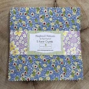 May include: A pack of 5 fabric squares with a floral print in shades of blue, yellow, green, and purple. The fabric squares are labeled "Pinnafores & Petticoats by Kaye England 5 Karat Crystals Wilmington www.wilmingtonprints.com"