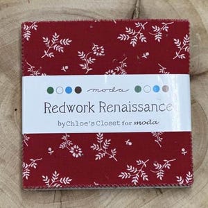 May include: A stack of red fabric squares with a white floral pattern. A white band wraps the squares, displaying the text "Redwork Renaissance" and "by Chloe's Closet for moda". The fabric is likely for quilting or crafting.