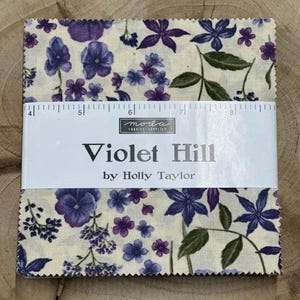 May include: A fabric square with a white background and a purple floral pattern. The fabric is labeled "Violet Hill by Holly Taylor" and is from Moda Fabrics & Supplies.