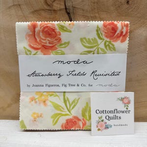 May include: A stack of fabric squares with a floral pattern featuring peach roses and green leaves. The fabric is labeled "Strawberry Fields Revisited" by Joanna Figueroa for Moda. A small square reads "Cottonflower Quilts, handmade."