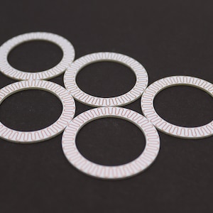 Pode incluir: Seis discos circulares brancos com uma borda vermelha estampada. Os discos estão dispostos em um padrão circular sobre um fundo preto.