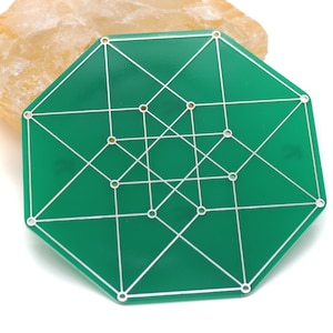 May include: A green, geometric game board with white lines and circles, set against a light-colored, textured background. The board has an octagonal shape and features a complex network of intersecting lines.