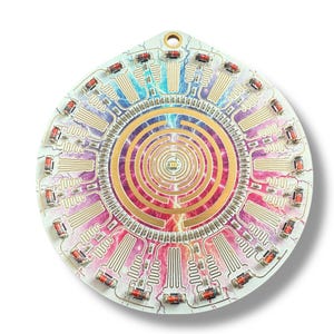 May include: A circular, multi-colored circuit board with a gold-colored, concentric circle pattern in the center. The board has a white background and is decorated with a rainbow of colors. The board is surrounded by a ring of small, red, rectangular components.