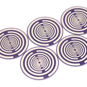 Può includere: Cinque circuiti stampati rotondi, con bordo viola, stampati in bianco e oro con un motivo a cerchi concentrici.