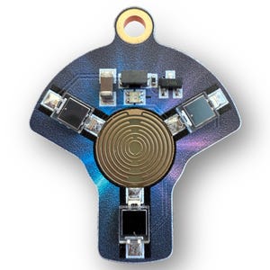 Può includere: Primo piano di un circuito stampato dalla forma unica. La scheda è principalmente blu scuro con un componente circolare dorato al centro. Diversi piccoli componenti neri sono disposti attorno al cerchio dorato.