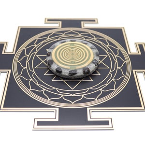 May include: A black and gold geometric design with a circular stone centerpiece. The stone has a gold spiral pattern and is surrounded by black stones. The design is on a white background.