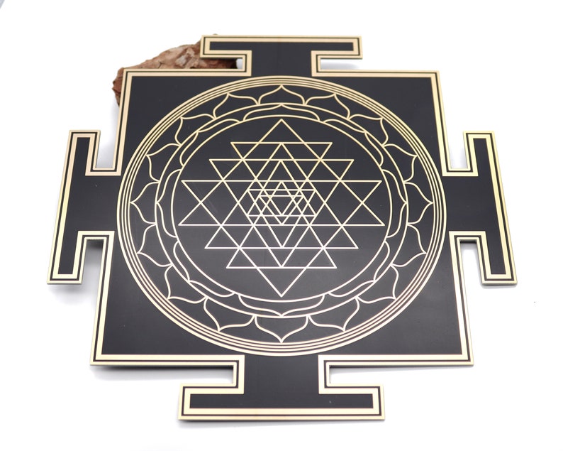 May include: A black and gold Sri Yantra, a geometric design with interlocking triangles and a lotus flower border. The design is set against a black background with gold accents. The object is a square shape with protruding rectangular elements.