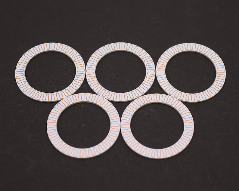 May include: Five white circular rings with a copper-colored pattern around the edge. The rings are arranged in a semi-circle pattern.
