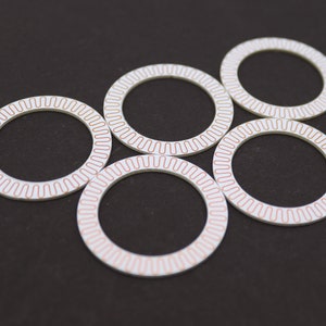 May include: Five white circular rings with a copper-colored design. The rings are arranged in a circle with the top ring slightly offset.