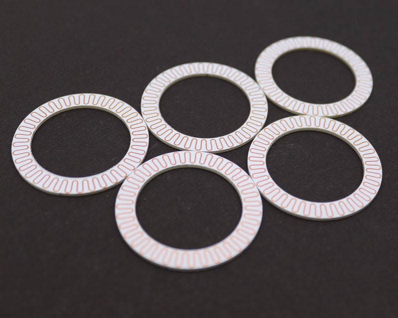 May include: Five white circular rings with a copper-colored design. The rings are arranged in a circle with the top ring slightly offset.