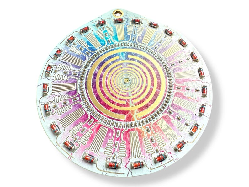May include: A circular circuit board with a colorful, rainbow-like design. The board features a central spiral pattern with a gold-colored maze. The board is surrounded by a ring of red LED lights.