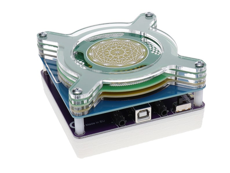 May include: A clear acrylic case with a green circuit board inside. The circuit board has a geometric pattern and the text "Made in EU" is visible on the case.