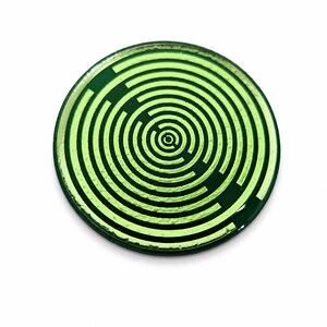 May include: A circular coaster featuring a vibrant lime green and dark forest green concentric maze pattern. The design consists of alternating circular lines that form a labyrinthine graphic, creating a high-contrast visual effect on the flat surface.