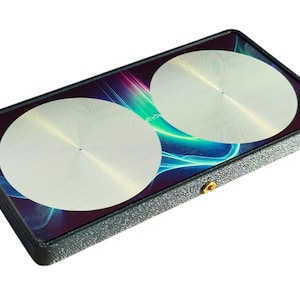 Può includere: Una custodia rettangolare nera con due dischi circolari argentati sulla parte superiore. La custodia presenta un design astratto colorato con striature blu, verdi e viola.