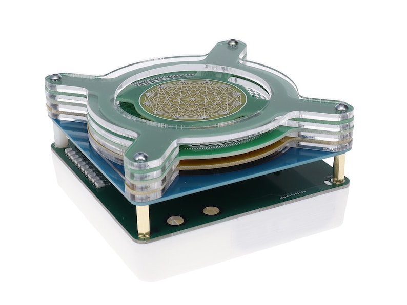 May include: A clear acrylic case with a green circuit board and a gold-colored circular component with a geometric pattern. The case is layered and has a white base.