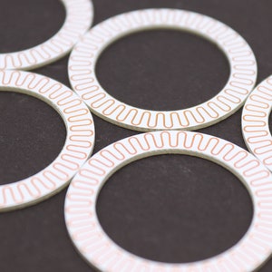 May include: Five white circular rings with a copper-colored line around the edge. The rings are arranged in a circle, with the copper-colored lines facing outward.