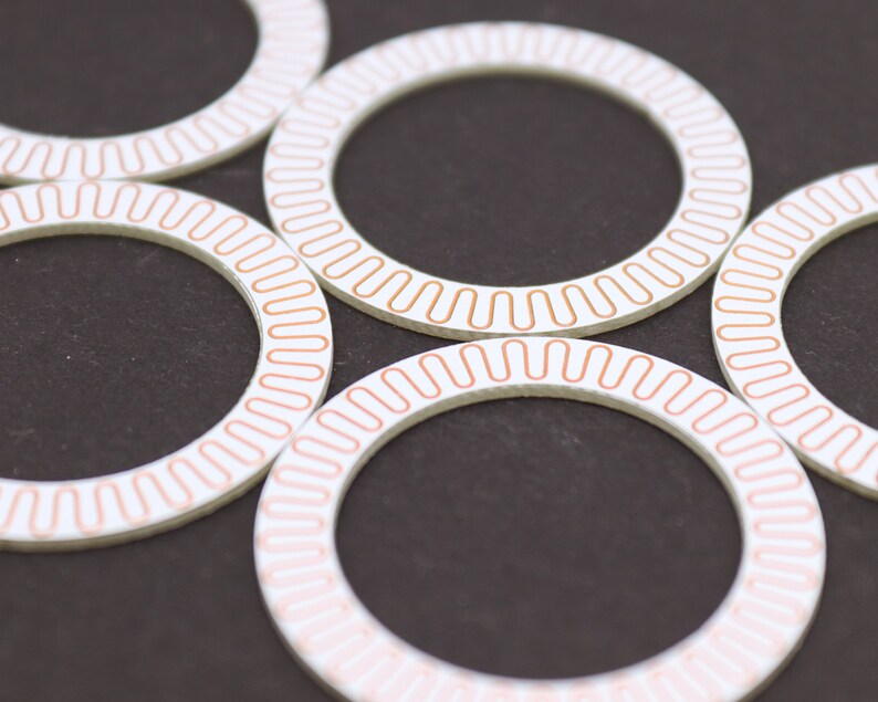 May include: Five white circular rings with a copper-colored line around the edge. The rings are arranged in a circle, with the copper-colored lines facing outward.