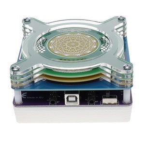 May include: A clear acrylic case with a circuit board inside. The board has a USB port, a power jack, and a switch. The case has a green and blue design. The text "Made in EU" is printed on the case.