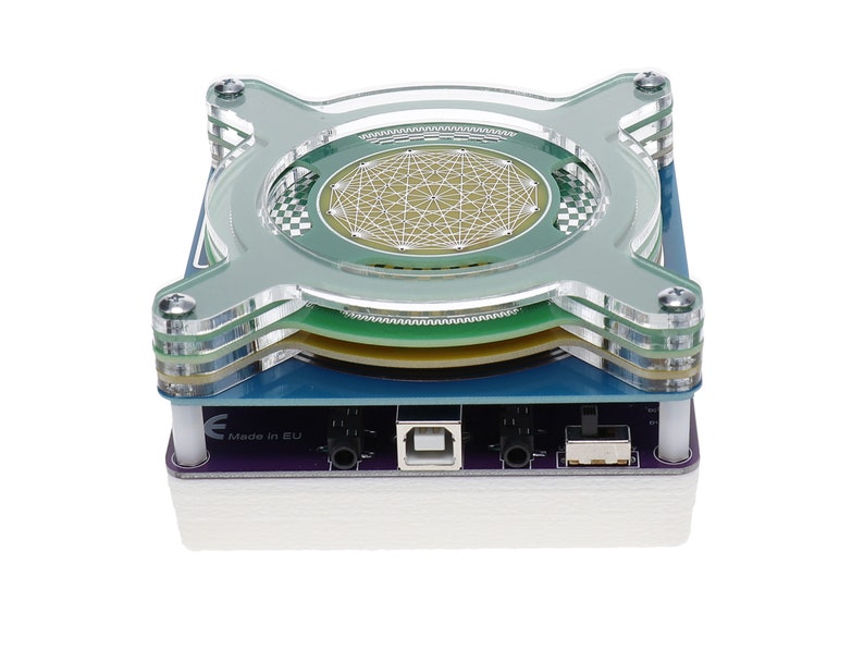 May include: A clear acrylic case with a circuit board inside. The board has a USB port, a power jack, and a switch. The case has a green and blue design. The text "Made in EU" is printed on the case.