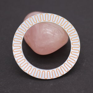 May include: A white circular bezel with a copper-colored ring of small ovals around the edge.