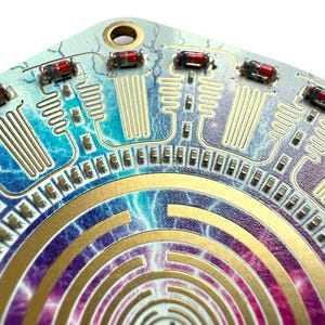 May include: A circular circuit board with a gold maze pattern and a blue, purple, and pink background. The board has multiple red and black resistors and a gold-colored metal ring around the center.