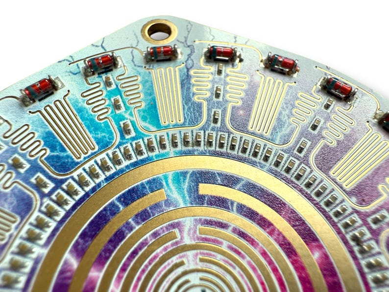 May include: A circular circuit board with a gold maze pattern and a blue, purple, and pink background. The board has multiple red and black resistors and a gold-colored metal ring around the center.