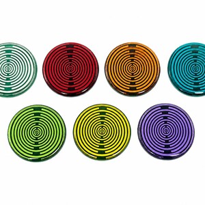 May include: Seven circular coasters in green, red, orange, teal, lime green, yellow, and purple. Each coaster features a black concentric circle pattern with a central dot and two vertical lines intersecting the rings, creating a target-like design.