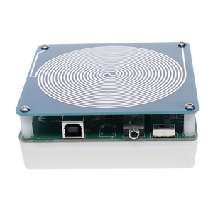 Può includere: Un'antenna a bobina circolare bianca e blu su un circuito stampato verde con una porta USB, un jack da 3,5 mm e un interruttore. La scheda è montata su una base bianca.