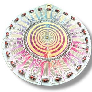 May include: A circular electronic circuit board with a colorful, abstract design. The board features a central spiral pattern and multiple red components around the edge.