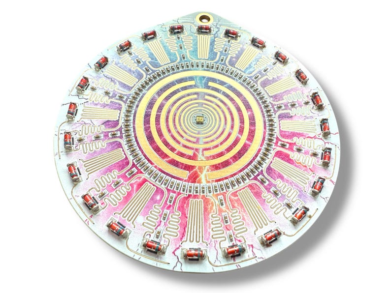 May include: A circular electronic circuit board with a colorful, abstract design. The board features a central spiral pattern and multiple red components around the edge.