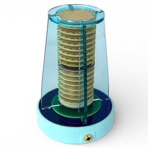 May include: A light blue and clear cylindrical device with a series of stacked, circular components inside a transparent enclosure. The base is light blue with a gold-colored jack. The top is also light blue.