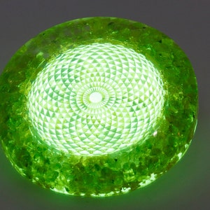 May include: A glowing, circular decorative object with a bright green hue. The center features a geometric pattern, surrounded by a textured, light green border. The object emits a soft, internal light, creating a captivating visual effect.