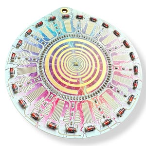May include: A circular circuit board with a colorful, swirling pattern and a central spiral design. The board is surrounded by a ring of small, red electronic components.