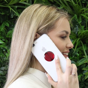 Może przedstawiać: Biały iPhone z czerwoną i czarną przyczepną podpórką do telefonu z tyłu.