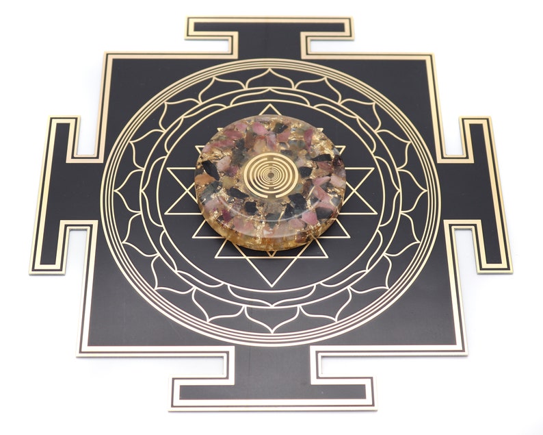 May include: A black and gold geometric design with a central circular object. The circular object is a mix of pink, black, and gold materials. The design features intricate patterns and shapes, creating a visually appealing and spiritual aesthetic.