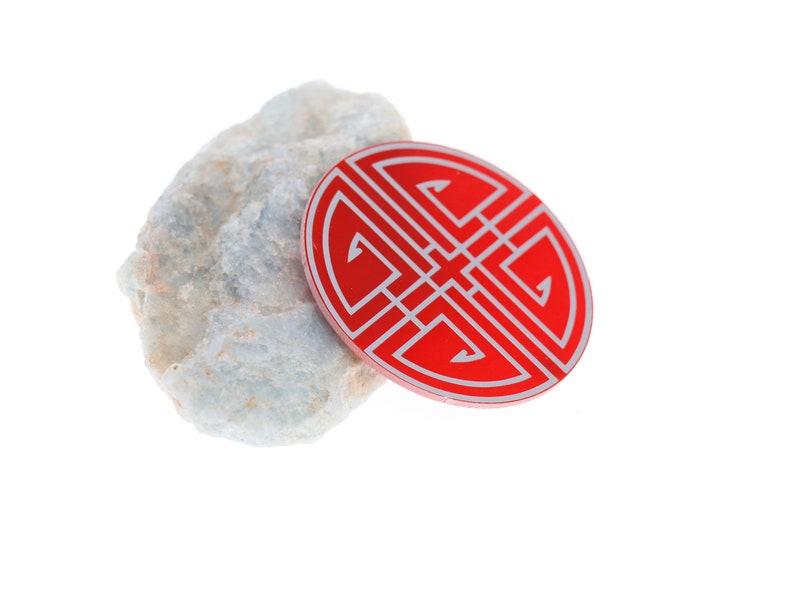 May include: A red and white circular charm with a traditional Chinese knot design, resting on a light blue rock.