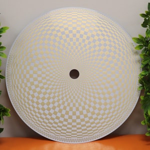 May include: A white circular disc with a gold checkered pattern radiating outward from the center. The center of the disc has a small black circle.