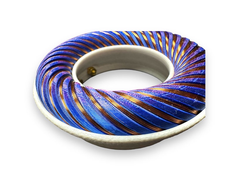 Peut inclure: Gros plan d'une bobine de couleur bleue et cuivre, enroul&eacute;e en spirale. La bobine est mont&eacute;e sur une base blanche.