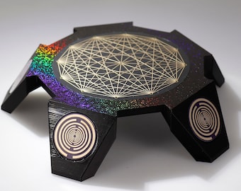 May include: A black, multi-sided, geometric platform with a rainbow iridescent finish. The platform has a gold geometric design in the center and a circular pattern on each of the sides.