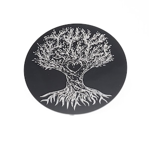 May include: A black circular coaster featuring a silver tree of life design. The tree has a heart at the centre of its trunk and detailed branches and roots.