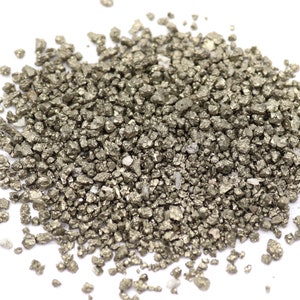 Op de afbeelding: Een stapel kleine, onregelmatig gevormde pyrietstenen. De stenen hebben een metallic, goudachtige uitstraling met een enigszins ruwe textuur. De pyrietstukken zijn verspreid tegen een witte achtergrond.